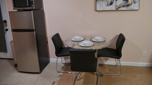 Een kleine keuken met een koelkast, magnetron en een eettafel met vier stoelen.