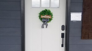 Una puerta blanca con un cartel de 'welcome', una figurita de perro y un felpudo.