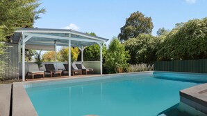 A swimming pool with lounge chairs and a covered seating area. - Uralla | Lovely house with pool (West Bathurst)