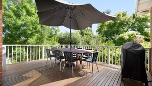 A wooden deck with a table and chairs under a large umbrella, surrounded by a white railing. - Uralla | Lovely house with pool (West Bathurst)