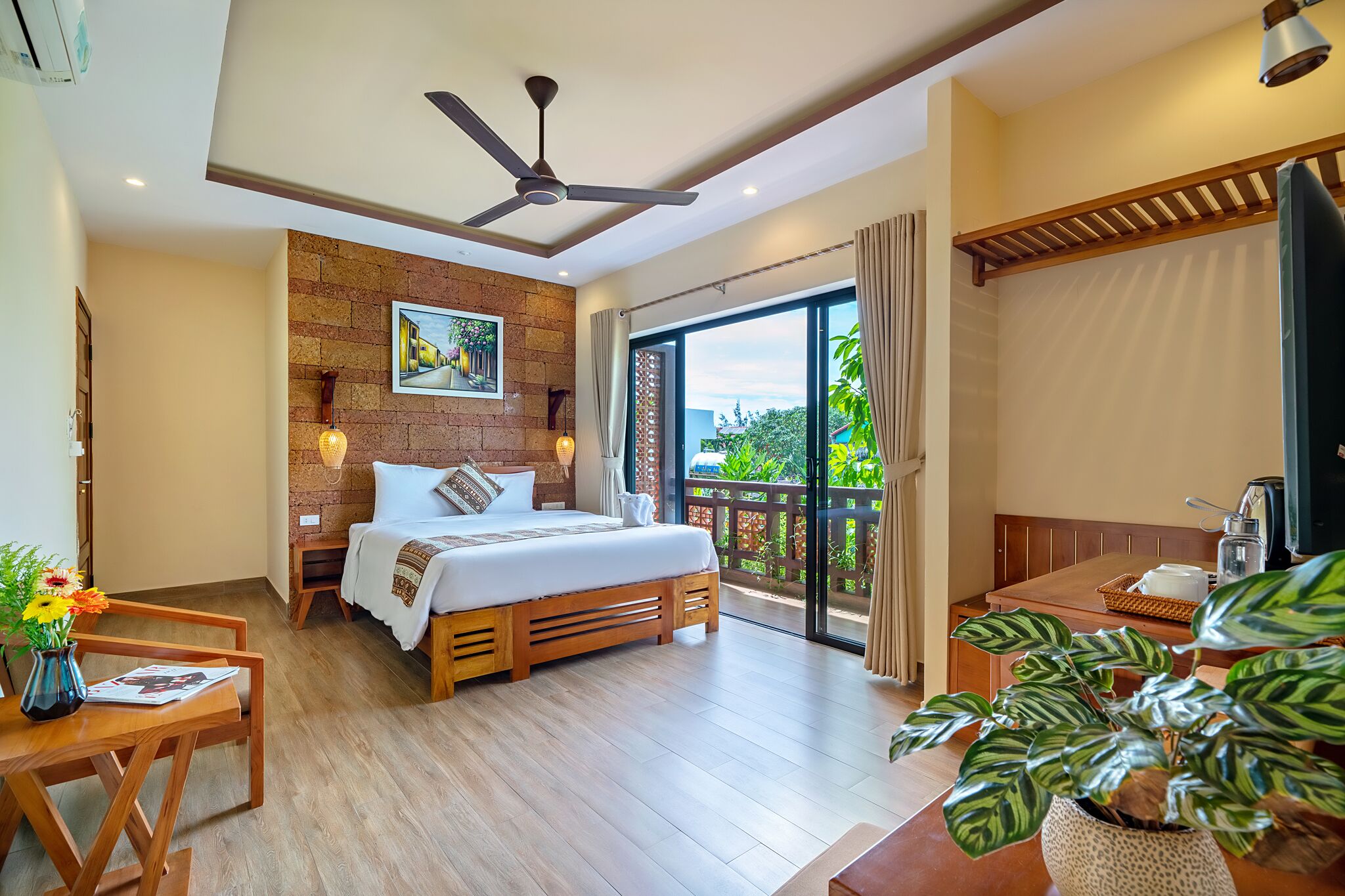 Habitación de hotel moderna con una cama grande, muebles de madera, un balcón con vistas y un ventilador de techo.
