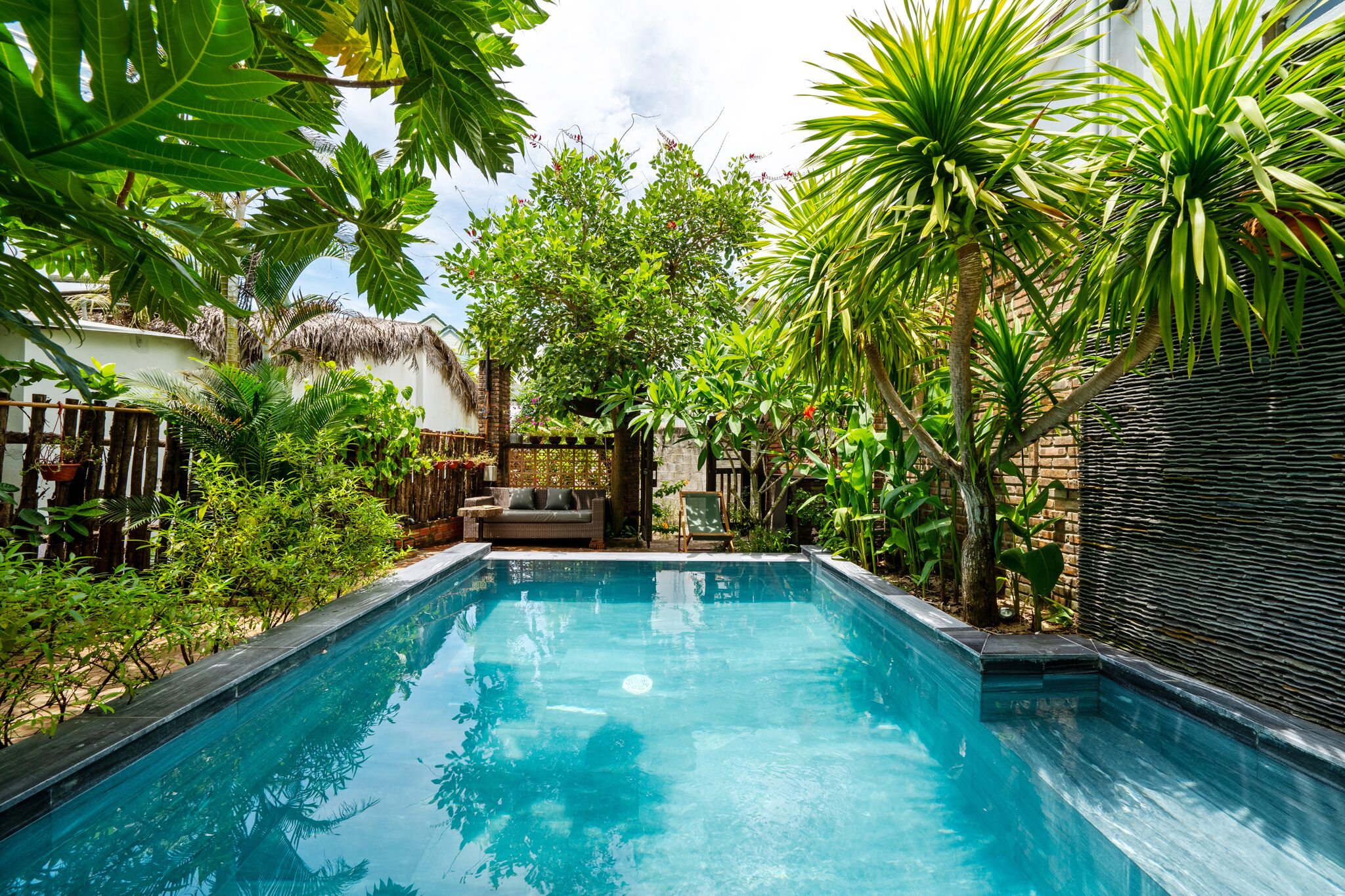 A swimming pool surrounded by lush tropical plants and a thatched-roof structure.
