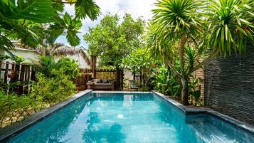 A swimming pool surrounded by lush tropical plants and a thatched-roof structure.