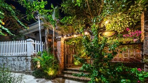 Entrada de jardí ben il·luminada amb un arc de maó, una valla de palets blancs i vegetació abundant.
