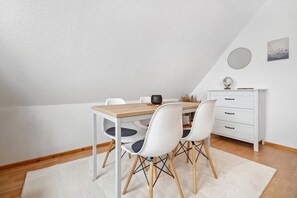 A dining area with a wooden table, white chairs, a white cabinet, and a globe on top. - Apartment "am Hainich" with Private Balcony & Wi-Fi (Craula)