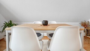 Una mesa de comedor con sillas blancas, un cuenco de cerámica oscura y una planta en maceta.