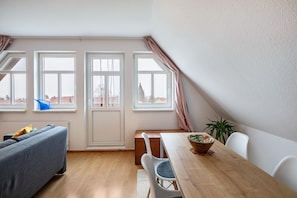 Ein Zimmer mit Esstisch, Stühlen, einer Couch und Fenstern.