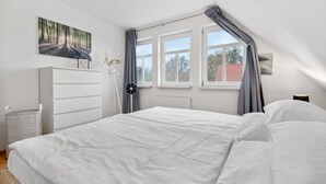 Un dormitorio con cama, cómoda, radiador, ventana con cortinas y un cuadro en la pared.