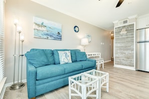 A living room with a teal sofa, white coffee table, and a painting of a beach scene.