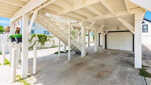 Ein überdachter Außenbereich mit Betonboden, weißen Säulen und einer Treppe, die zu einer Garage führt.
