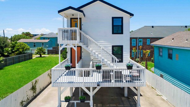 A two-story house with a white exterior, a balcony with white railings, and a small porch area. - Modern dog-friendly duplex, 1 block from beach with shared backyard patio & W/D (Galveston)