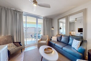 Relax in this spacious living room with a sofa set, coffee table, and armchairs, featuring a large window with an outside view and a flat-screen TV.
