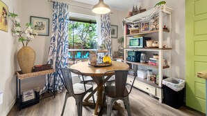 Un comedor con una mesa redonda, sillas, una lámpara colgante, una estantería y un ventanal con cortinas.