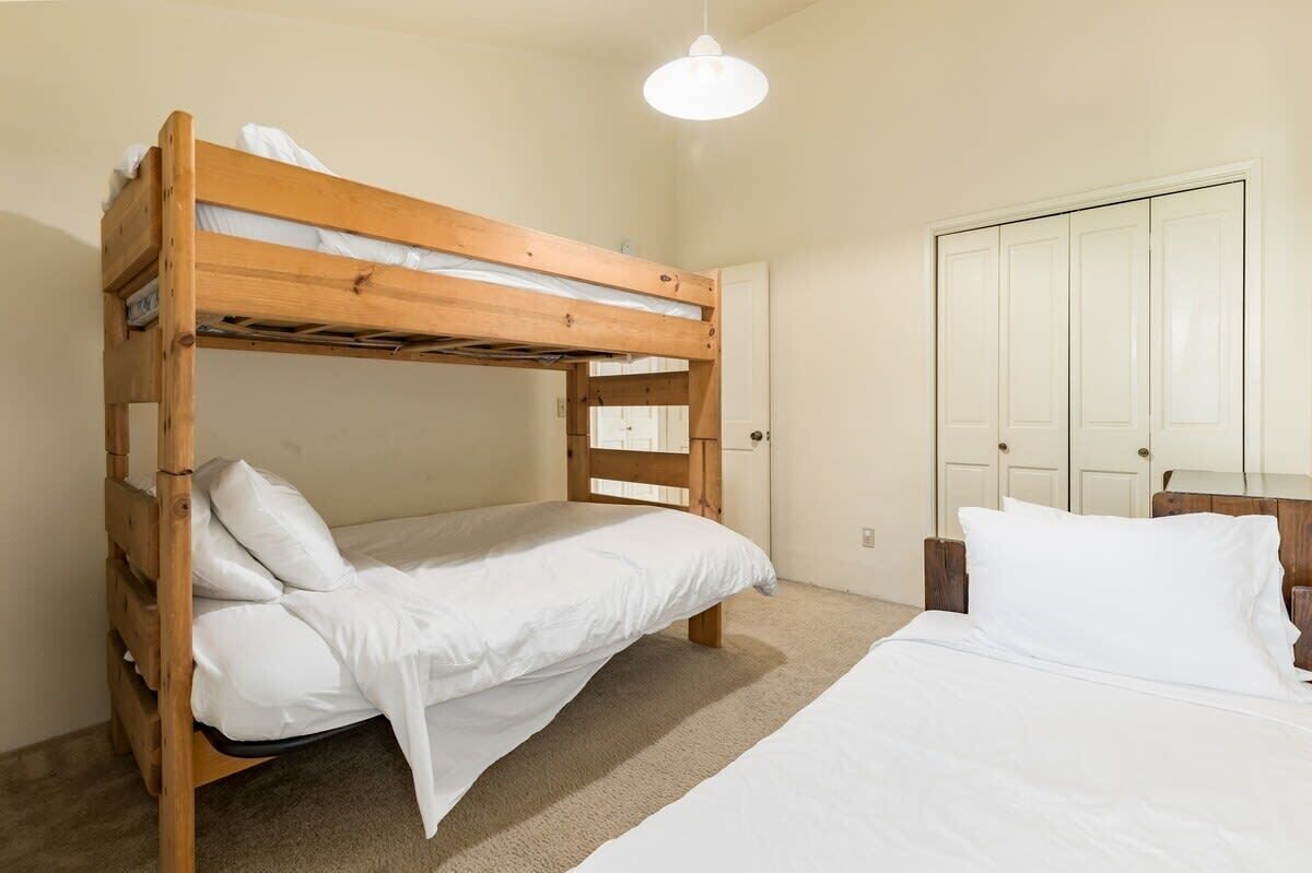A bunk bed with white bedding, a wooden headboard, a white door, and a hanging light fixture.