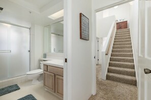 A bathroom with a toilet, sink, and mirror. There is a staircase leading to another room.