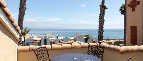Un balcone con tavolo e sedie in vetro, vista sulla spiaggia e sul mare.
