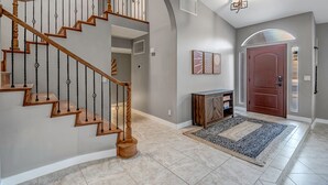 A spacious foyer with a wooden staircase, a fireplace, and a large door.