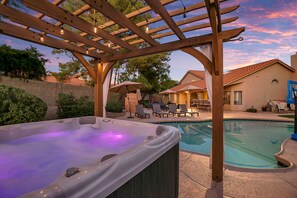 Ein Whirlpool unter einer Holzpergola mit einem Pool und Gartenmöbeln.