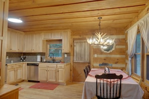 A wooden cabin interior with a kitchen, dining area, and a chandelier. - Cozy Cabin with ADA accessible, golfing, hiking,, beach, tennis, and more! (Jasper)