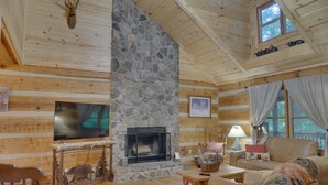 L’intérieur d’une cabane en rondins, avec une cheminée en pierre, des meubles en bois et une tête de cerf accrochée au mur.