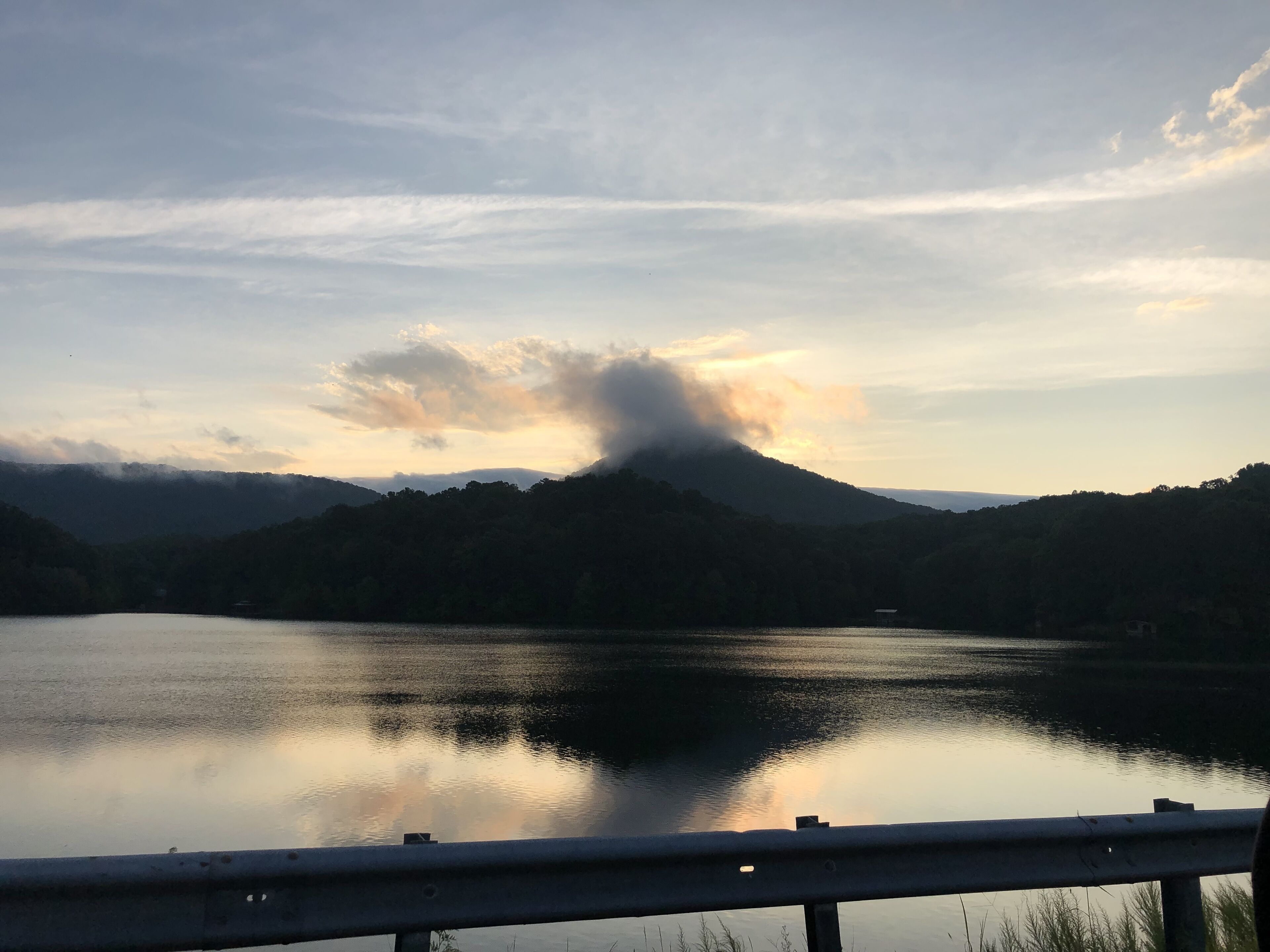 A calm lake with a mountain in the background and a cloudy sky.