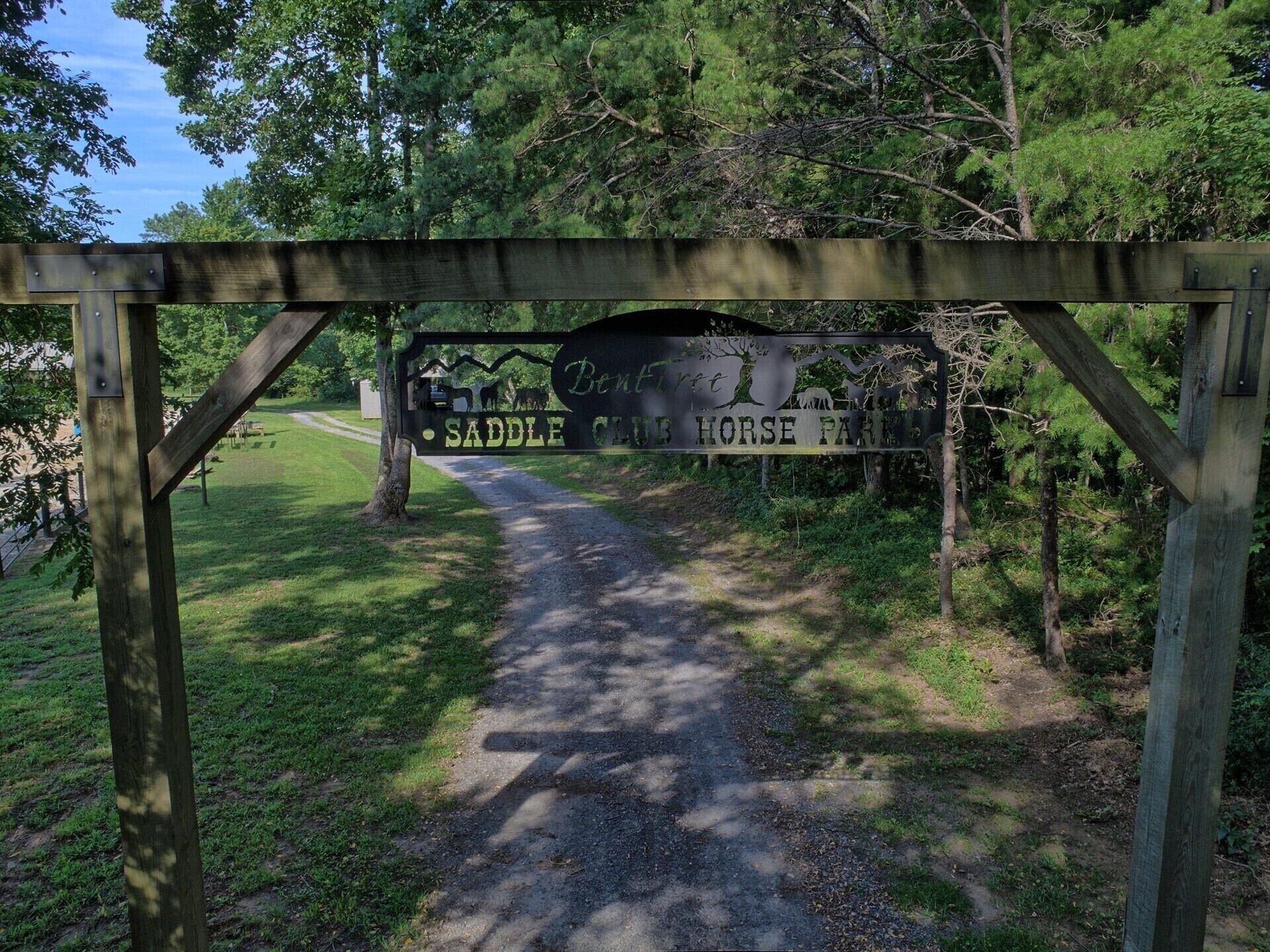 A wooden sign for Saddle Club Horse Park with a path leading through a wooded area.