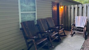 Een houten terras met twee schommelstoelen en een houten bank, een deur en een raam met zonwering.