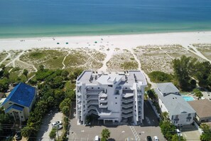 A multi-story hotel with a central courtyard, surrounded by a beach and sparse vegetation.