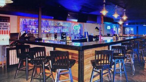 Eine Bar mit Sitzhocker, einer Theke und Regalen voller Flaschen.