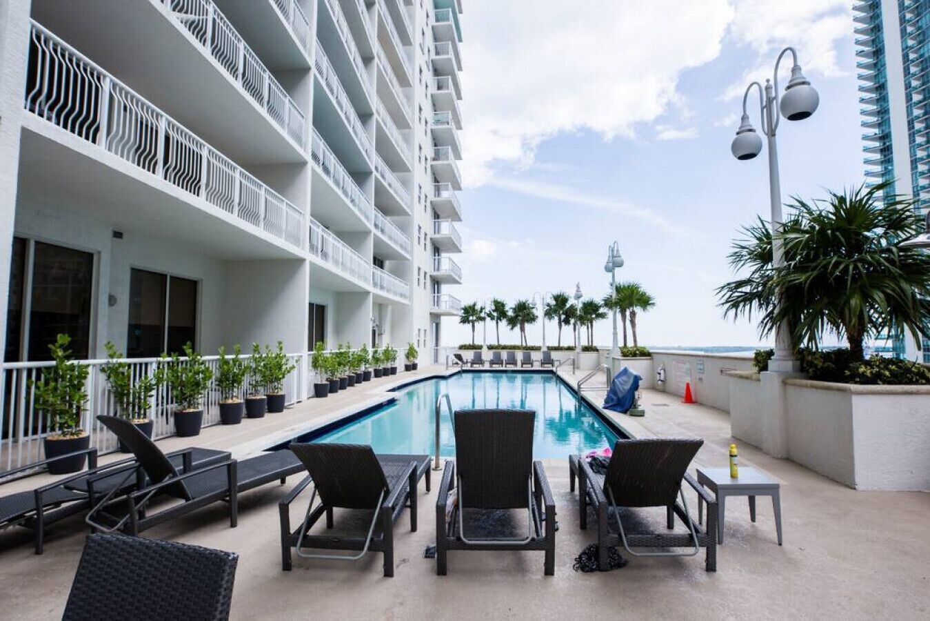 A rooftop pool area with lounge chairs and potted plants, overlooking a body of water.