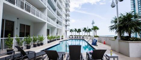 A rooftop pool area with lounge chairs and potted plants, overlooking a body of water.