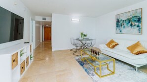 A modern living room with a white sofa, a glass coffee table, and a flat-screen TV on a white cabinet. - TC-3406 · Lovely 2BR Rental in the Heart of Brickell (Miami)