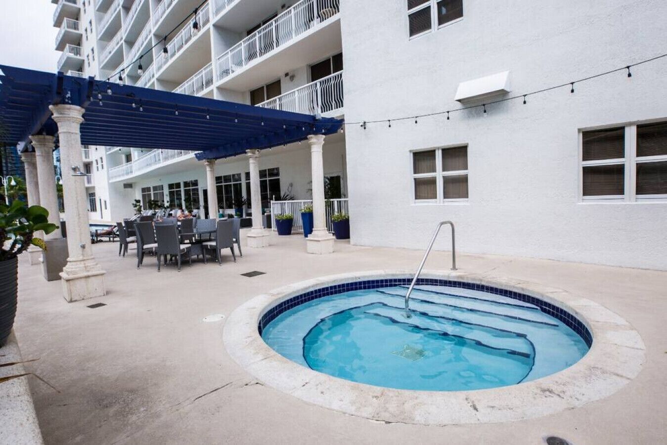 An outdoor pool area with a blue-tiled pool, outdoor seating, and a covered patio area.