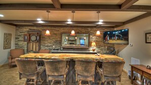 A bar area with a long wooden table, multiple bar stools, and a stone wall backdrop. - Hot tub, firepit, outdoor living, comfy beds, and more! - 5 O'Clock Somewhere (Mineral Bluff)