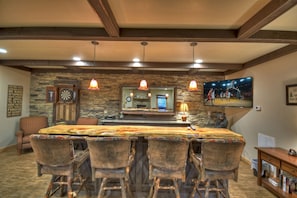 Un espace bar avec une longue table en bois, de nombreux tabourets de bar et un mur en pierre en arrière-plan.