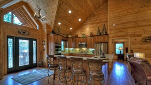 A spacious log cabin interior with a large kitchen, wooden floors, and a bar area with stools. - Hot tub, firepit, outdoor living, comfy beds, and more! - 5 O'Clock Somewhere (Mineral Bluff)