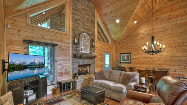 A log cabin interior with a fireplace, a large flat-screen TV, leather furniture, and a chandelier. - Hot tub, firepit, outdoor living, comfy beds, and more! - 5 O'Clock Somewhere (Mineral Bluff)