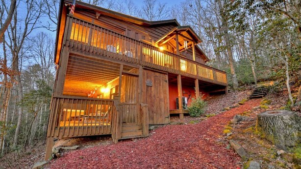 Eine Holzhütte mit Balkon, umgeben von Bäumen und einem mit roter Rindenmulch bedeckten Waldboden.