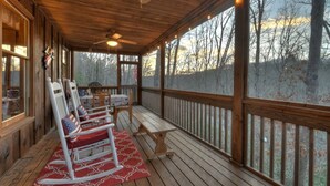 Eine überdachte Veranda mit Schaukelstühlen, einem Tisch und Blick auf Bäume.