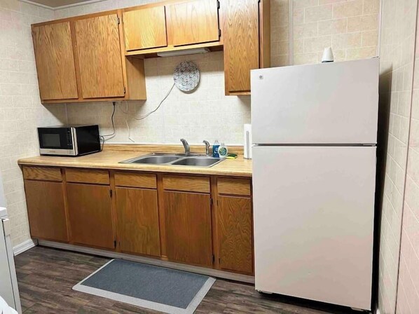 A compact kitchen with wooden cabinets, a microwave, a sink, and a white refrigerator.