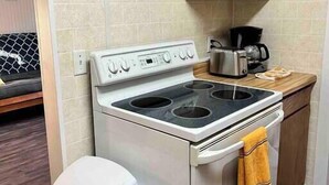 A compact kitchen with a stainless steel stove, wooden cabinets, and a small trash bin.