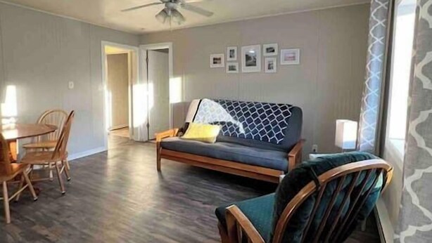 A spacious living room with a dark wood floor, a sofa with a patterned cover, a wooden chair, and a dining table with chairs.