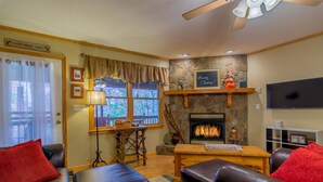 A cozy living room with leather sofas, a fireplace, a stone wall, and a television.