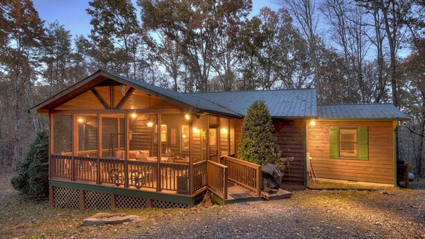 A cabin with a deck, a small attached building, and a forested backdrop.