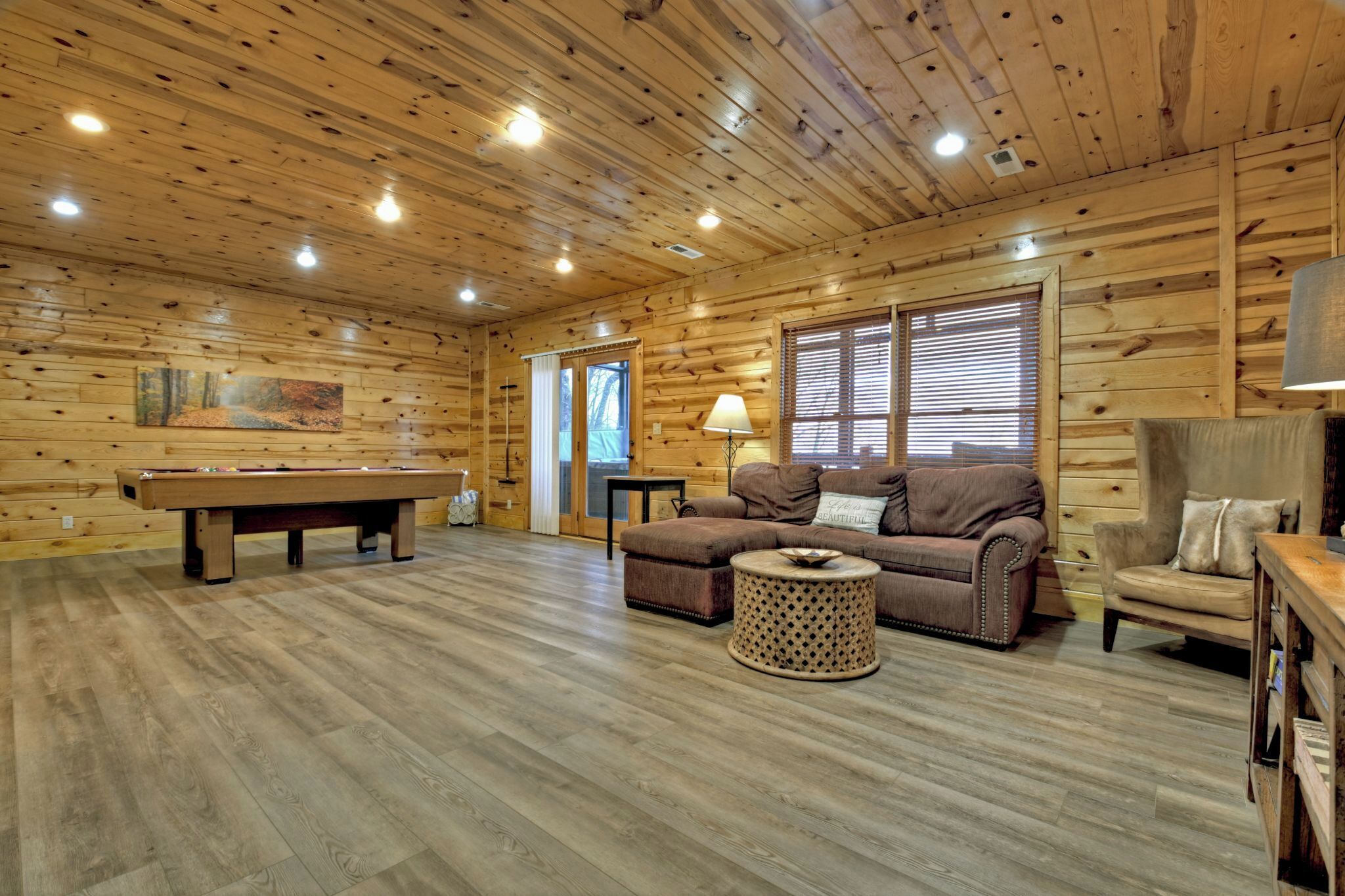 A cozy room with a pool table, a sofa, a chair, and a lamp.