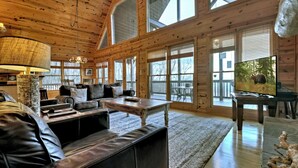 A spacious log cabin interior with a large wooden ceiling, a leather sofa, a wooden coffee table, and a television on a stand. - Nearby hikes + a hot tub! - Appalachian Sunrise (Blue Ridge)