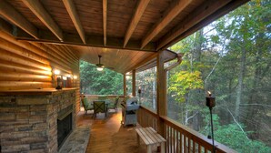 A wooden deck with a stone fireplace, outdoor seating, and a view of a forest. - Nearby creek, cozy hot tub, pool table, and more! - Castle Creek (Cherry Log)