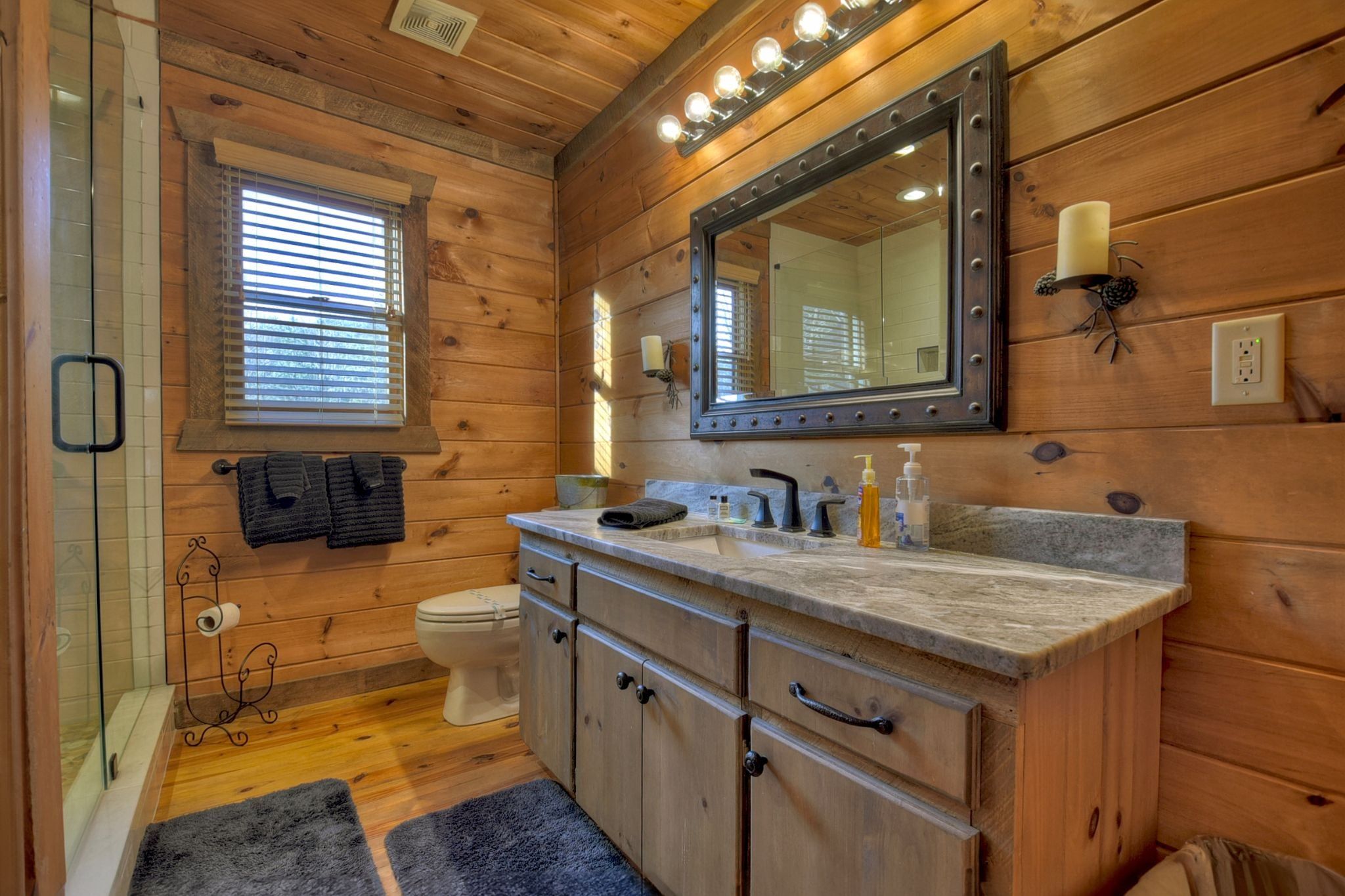 Une salle de bain rustique, aménagée dans une cabane en bois, avec un meuble-lavabo, un évier, un miroir et des toilettes.