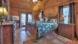 A wooden cabin bedroom with a bed, dresser, and a ceiling fan. - Nearby creek, cozy hot tub, pool table, and more! - Castle Creek (Cherry Log)