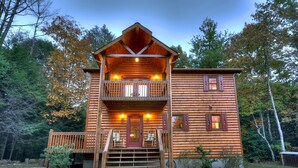 A log cabin with a balcony, a front porch with chairs, and a gravel driveway. - Nearby creek, cozy hot tub, pool table, and more! - Castle Creek (Cherry Log)